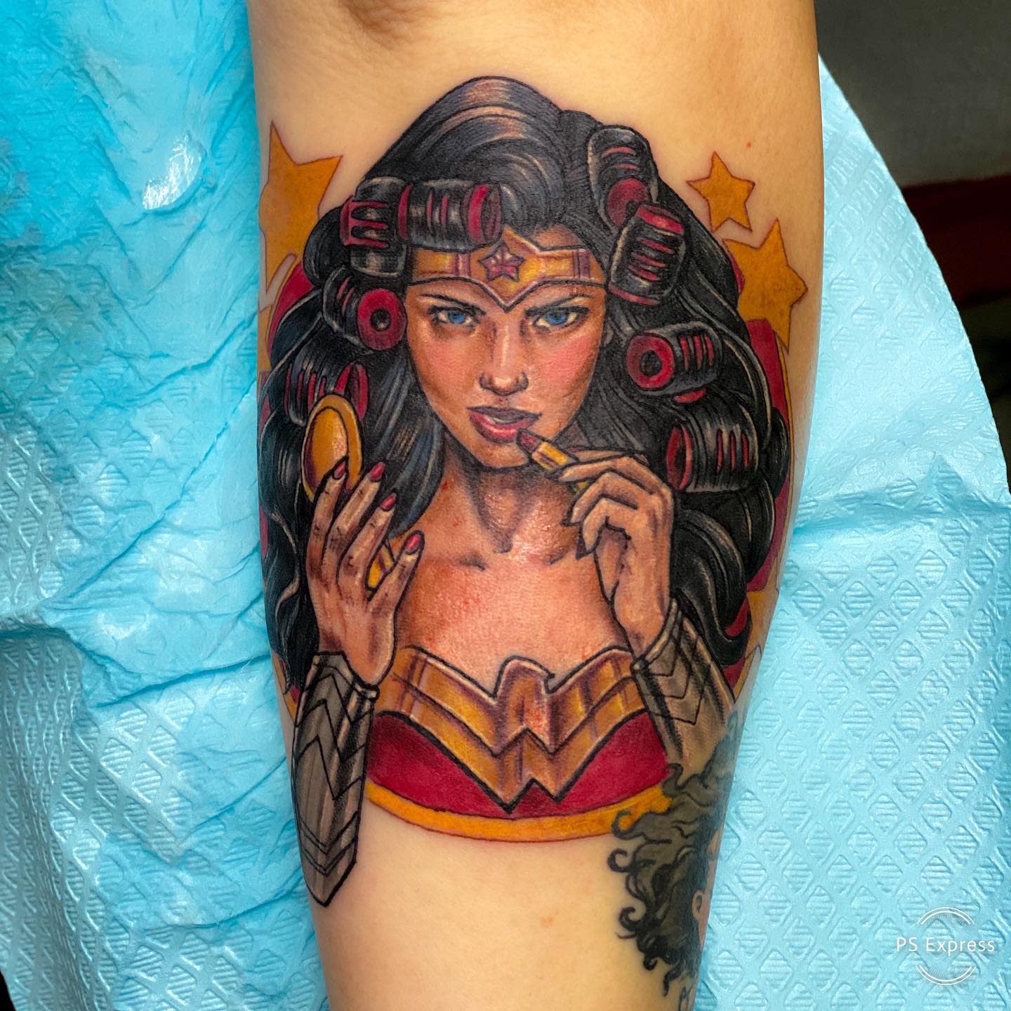 Wonder Woman tattoo in new school style, applying lipstick with hair in rollers, blending strength and femininity